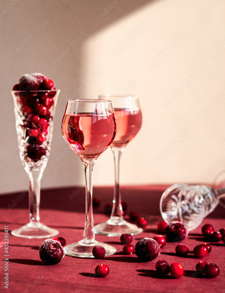 red berries scattering from a crystal glass lying on the table among glasses with pink alcoholic drink, light and shadow, cranberry's or cherry's vodka, liqueur red berries scattering from a crystal glass lying on the table among glasses with pink alcoholic drink, light and shadow, cranberry's or cherry's vodka, liqueur
