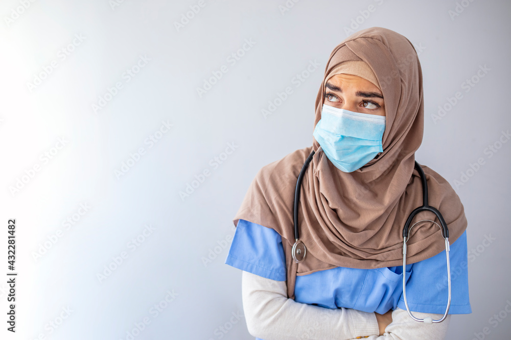 Stressed muslim woman doctor in protective face mask touching her sweating forehead, feeling exhausted after difficult working day, sitting by wall at clinic, copy space. Doctors and COVID-19 pandemic Stressed muslim woman doctor in protective face mask touching her sweating forehead, feeling exhausted after difficult working day, sitting by wall at clinic, copy space. Doctors and COVID-19 pandemic