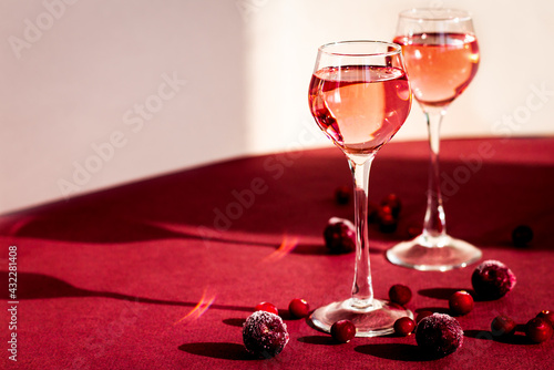 two glasses of pink gin or vodka infused with cranberry among frozen berries, cherry liqueur or any red alcoholic cocktail closeup, a pair of long-stemmed glasses, copy space