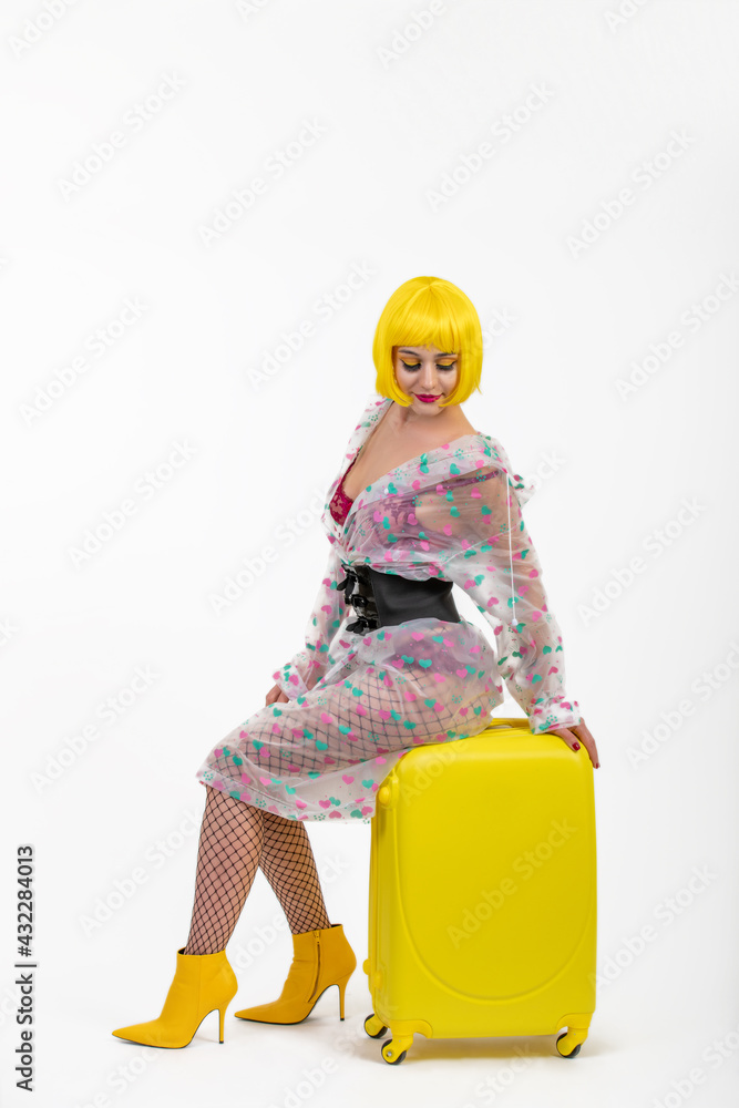 Stylish woman in yellow wig sitting on suitcase isolated on white background. travel cocept Stylish woman in yellow wig sitting on suitcase isolated on white background. travel cocept