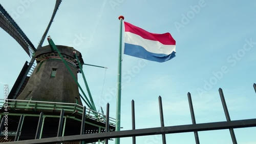 Dutch red, white and blue flag waving in the wind with an old dutch windmill and blue sky in the background during a sunny day. Slow-motion clip. photo