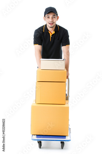 Overjoyed Asian delivery man pushes hand truck with stack of cardboard boxes. Full length portrait of courier guy in black t-shirt uniform on white background. E-commerce business concept. photo