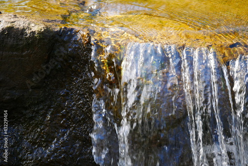 close up of a small waterfall with big wet stones in the sunlight
