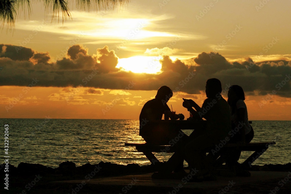 Silhouettes of people having drinks on a picnic table with a stunning sunset in a tropical island