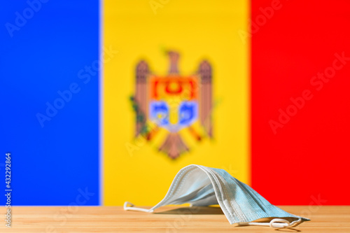 A medical mask lies on the table against the background of the flag of Moldova. The concept of a mandatory mask regime for residents of the country and tourists in Moldova during a pandemic.