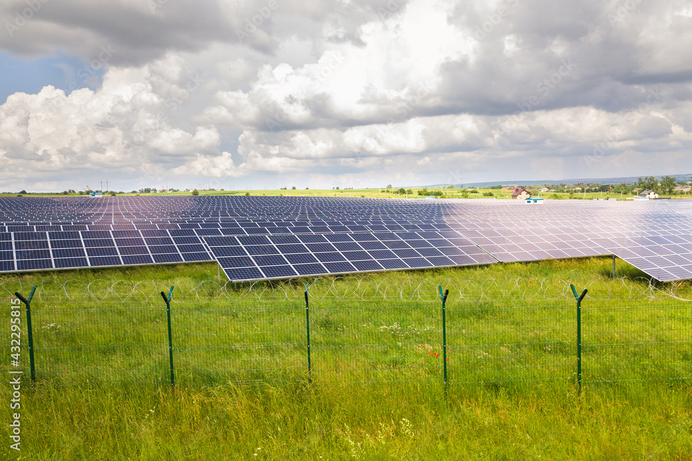 Aerial view of solar power plant on green field with protective wire fence around it. Electric panels for producing clean ecologic energy.