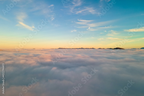 Aerial view of vibrant sunset over white dense clouds with distant dark mountains on horizon.
