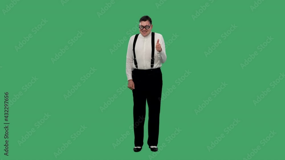 Portrait of a contented man dancing and showing a thumb up. A man in glasses with thick lenses, a white shirt with a suspender poses in the studio on a green screen. Slow motion.