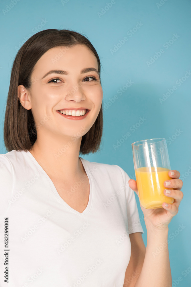 Young Caucasian woman drinking fresh orange juice isolated on blue background Young Caucasian woman drinking fresh orange juice isolated on blue background