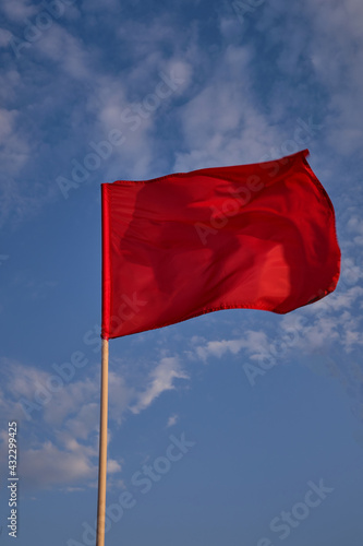 Red flag with blue sky with clouds, strong wind flying red flag. Red flag warning flags