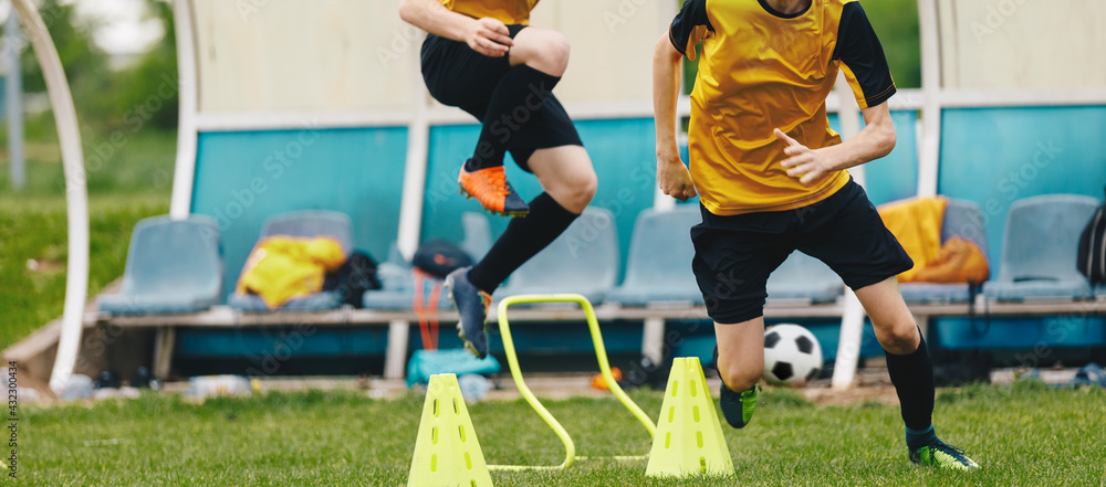Two young athletes on soccer training drill. Football camp practice activities for players. Two boys running on training football obstacle course Two young athletes on soccer training drill. Football camp practice activities for players. Two boys running on training football obstacle course