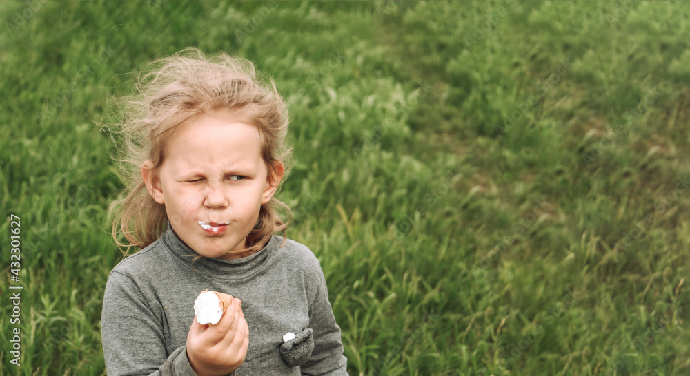 Portrait of a child in nature. Copy space. Beautiful blonde girl 4 years old. Green grass background. The child is eating cold ice cream. Portrait of a child in nature. Copy space. Beautiful blonde girl 4 years old. Green grass background. The child is eating cold ice cream.