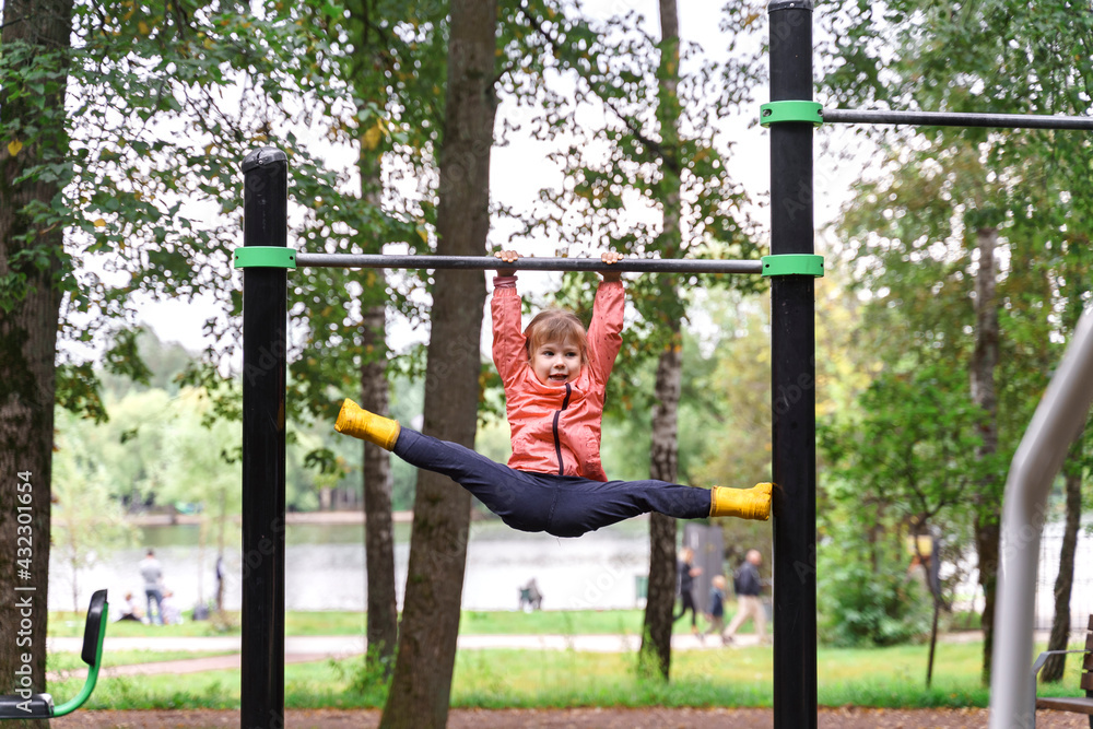 little girl doing twine on a horizontal bar in an autumn park little girl doing twine on a horizontal bar in an autumn park