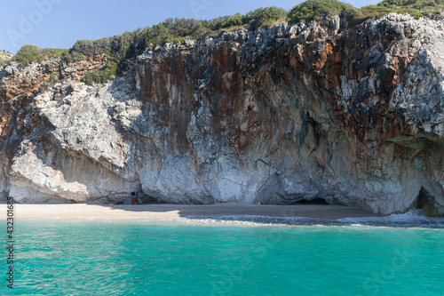 Turquoise sea, cliffs surrounded by green plants and a tourist tent on a small wild beach, Albania. Travel theme, beautiful nature