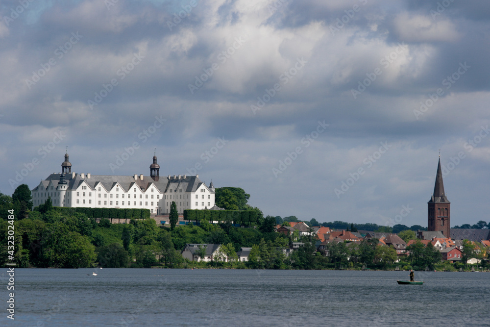 Lakeside view of the beautiful castle and church of Plön, Germany with cloudy sky in the background and sun shining on the landmark Lakeside view of the beautiful castle and church of Plön, Germany with cloudy sky in the background and sun shining on the landmark