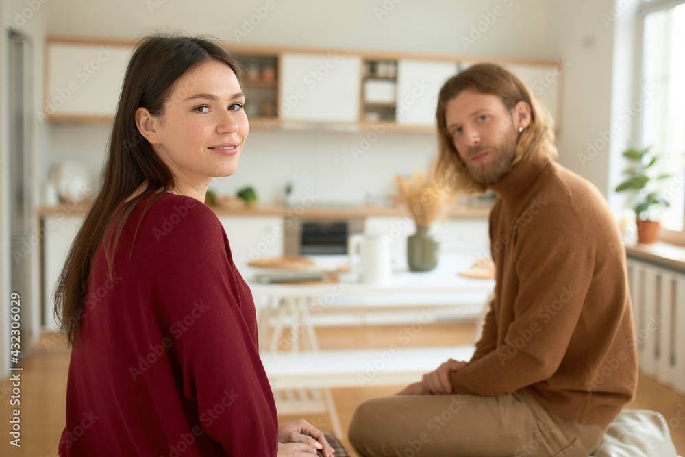 Beautiful young brunette female spending leisure time on weekend indoors together with her handsome unshaven husband looking at camera with happy smile. Family, marriage, home and domestic life Beautiful young brunette female spending leisure time on weekend indoors together with her handsome unshaven husband looking at camera with happy smile. Family, marriage, home and domestic life