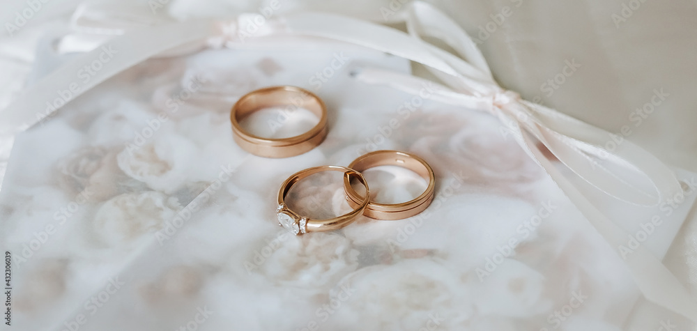 Two wedding rings and an engagement ring lie on an invitation with flowers background Two wedding rings and an engagement ring lie on an invitation with flowers background