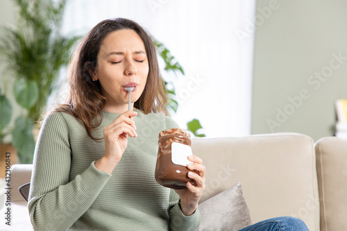 Tablou pe pânză Young woman eating chocolate from a jar at home.