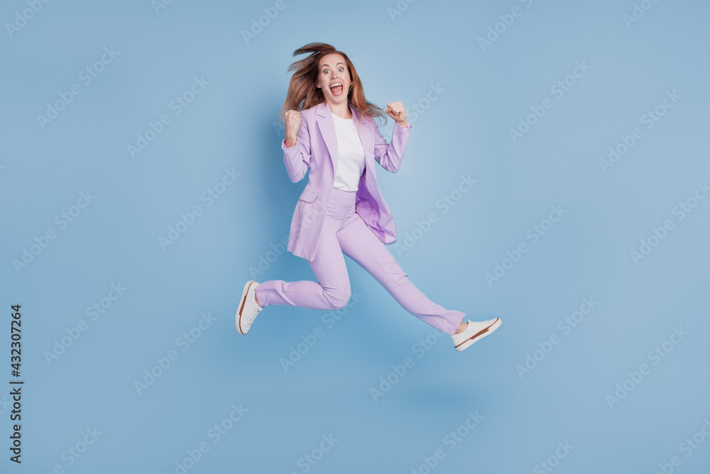 Photo of crazy surprised girl jump win raise fists isolated over blue background Photo of crazy surprised girl jump win raise fists isolated over blue background