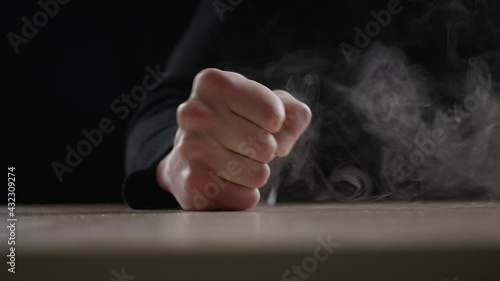 Close-up evil man beats his fist on the table showing aggression on dark background. Terrible man's fist with fury hitting the table. Concept of anger. Slow motion