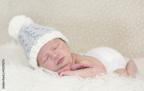 Adorable newborn Caucasian baby boy in bonnet sleeping on a white fur cloth photo