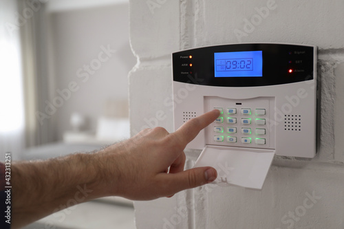 Man entering code on security alarm system at home, closeup photo