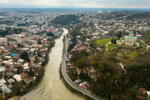 Scenic aerial view of Kutaisi cityscape on banks of Rioni River in spring overlooking medieval Bagrati Cathedral, Imereti region, Georgia. © JackF