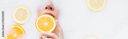 top view of woman holding orange slice in milk bath, banner.