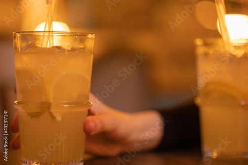 A glass with lemonade  lemon wedges  ice cubes. Summer cold refreshing drink  alcoholic cocktail in the hand of a man on the table in a bar. Close-up