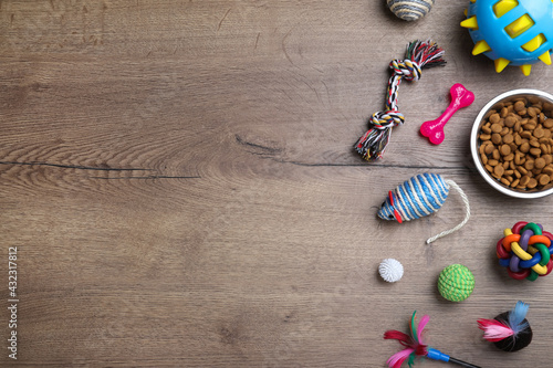 Flat lay composition with different pet toys and feeding bowl on wooden background, space for text