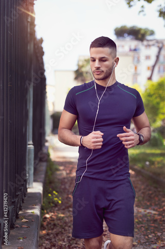 Young man jogging in an outdoor park. He runs with headphones while listening to music.