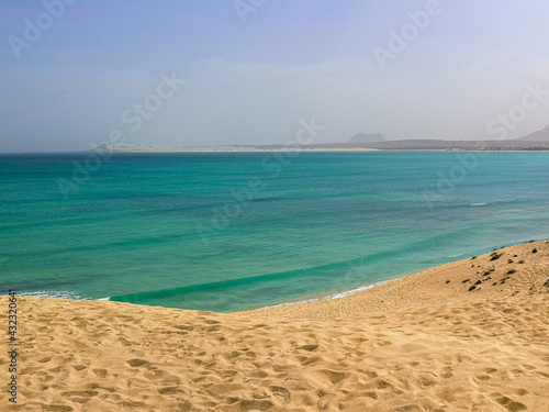 Atlantic Ocean view from a large sand dune  Boa Vista Island  Cape Verde. Clear blue water and a hot tropical day in Africa. Selective focus on the footprint pattern  blurred background.