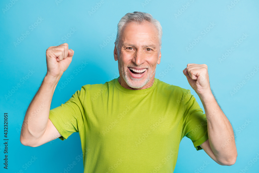 Photo of astonished positive man fists up toothy smile celebrate look camera isolated on blue color background Photo of astonished positive man fists up toothy smile celebrate look camera isolated on blue color background