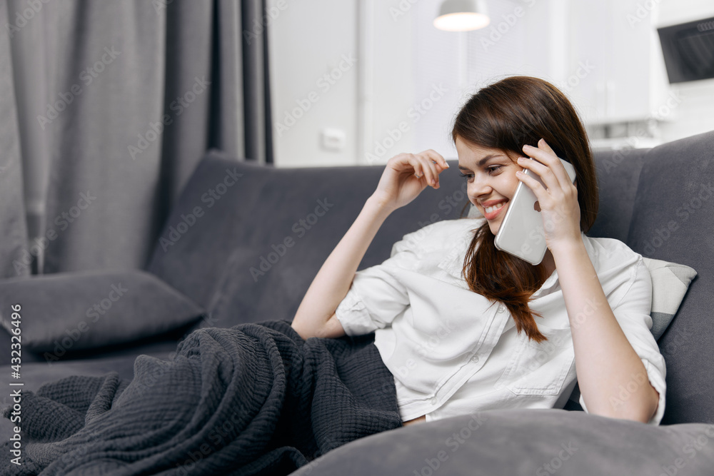 woman talking on the phone in a comfortable room hiding with a blanket on the sofa woman talking on the phone in a comfortable room hiding with a blanket on the sofa