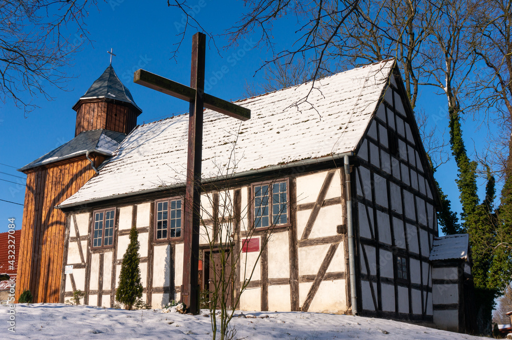 Half-timbered church Saint Matthew the Apostle dates from 1737 (Kościół św. Mateusza Apostoła). Wooden cross in front of the temple, the roof is covered with snow. Lobez County. Gardno, Poland.