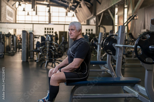 an elderly man in sportswear at a workout in a fitness club sits on a bench press getting ready for an exercise