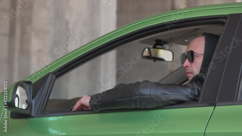 A man sitting in a car and taking a photo with a professional camera, a private detective or a paparazzi spy.