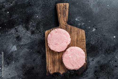 Uncooked Raw mince meat patty cutlet with herbs. Black background. Top view