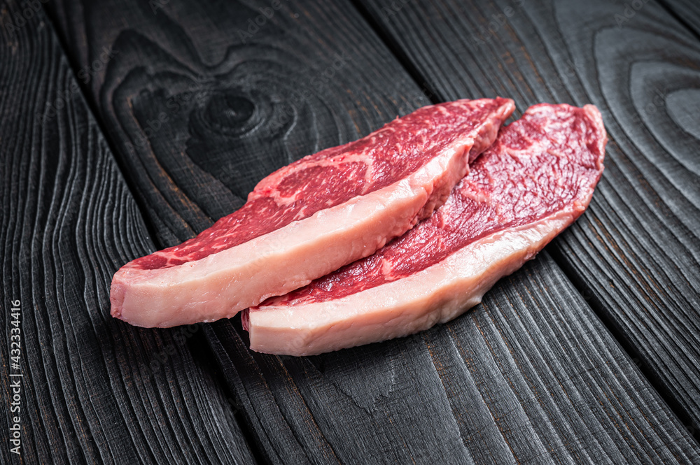 Raw rump steak or top sirloin cap beef meat steaks on butcher table. Black wooden background. Top view