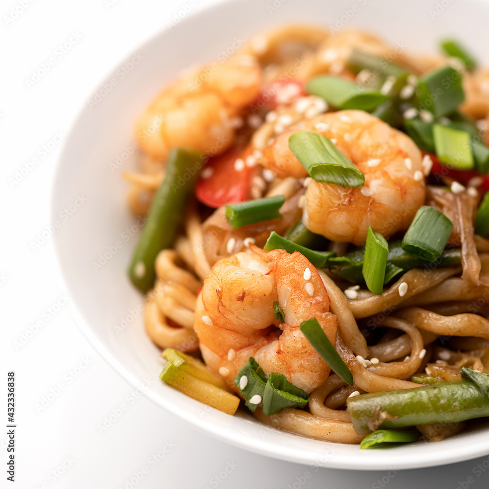 Wok noodles with shrimp or prawn, vegetables and sesame seeds. Spicy oriental dish, Pan-Asian cuisine. Part of food plate on white background. Soft focus. Close up shot. Wok noodles with shrimp or prawn, vegetables and sesame seeds. Spicy oriental dish, Pan-Asian cuisine. Part of food plate on white background. Soft focus. Close up shot.