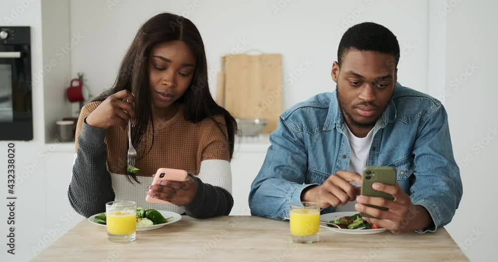 African American couple using mobile phone while having lunch at home African American couple using mobile phone while having lunch at home