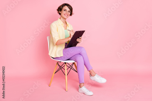 Photo of charming cute young woman wear yellow shirt glasses sitting chair signing documents isolated pink color background