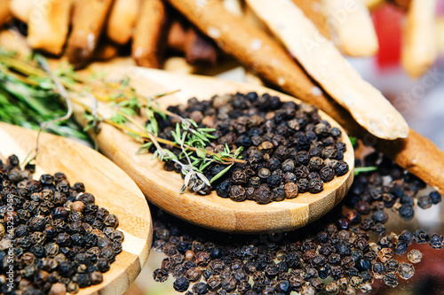 Black pepper on a wooden spoon. Seasonings for cooking various dishes, decorated with herbs. Close-up