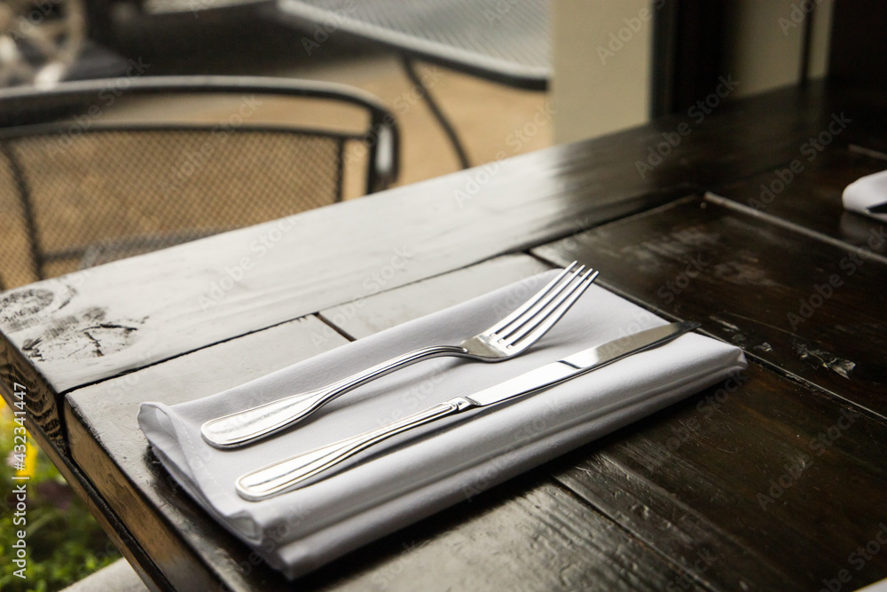 A silverware setting of a ffork and knife on a wood table at a high end restaurant near a window A silverware setting of a ffork and knife on a wood table at a high end restaurant near a window
