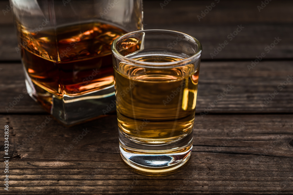 Glass of brandy and tequila on an old wooden table. Close up view, focus on the glass of tequila Glass of brandy and tequila on an old wooden table. Close up view, focus on the glass of tequila