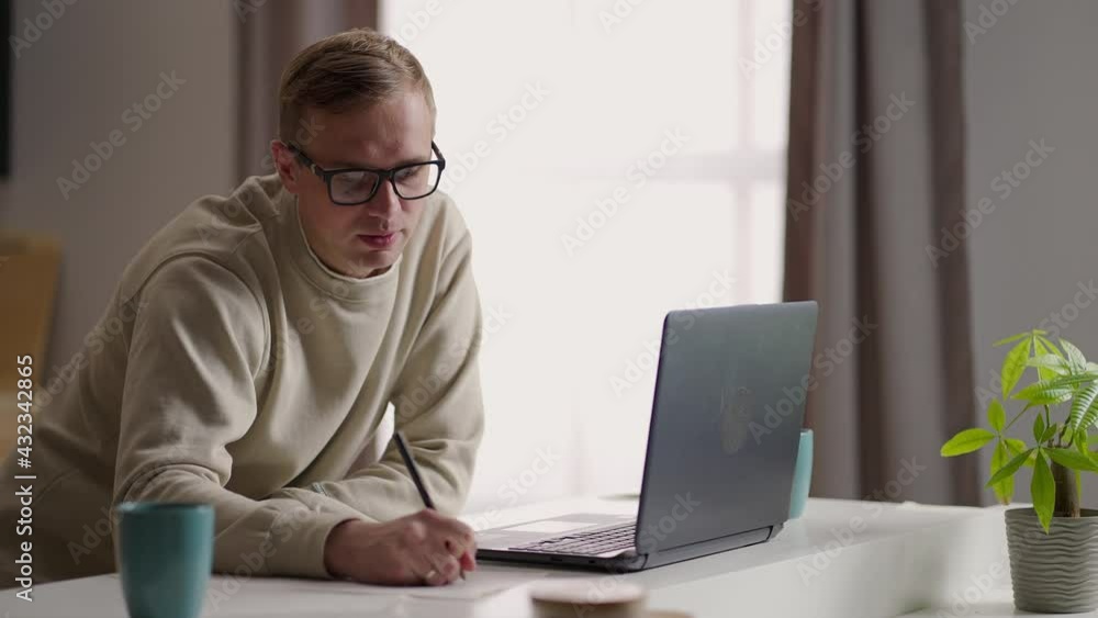 A man with glasses works from home in his kitchen using a laptop and the Internet. Remote work and remote learning A man with glasses works from home in his kitchen using a laptop and the Internet. Remote work and remote learning