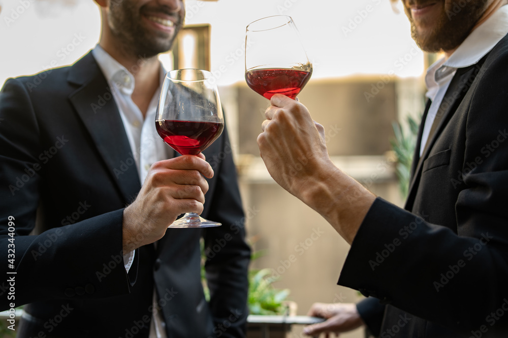 Two businessmen in suit standing in hotel room and talking together holding wineglasses with red wine and drinking together. Two businessmen in suit standing in hotel room and talking together holding wineglasses with red wine and drinking together.