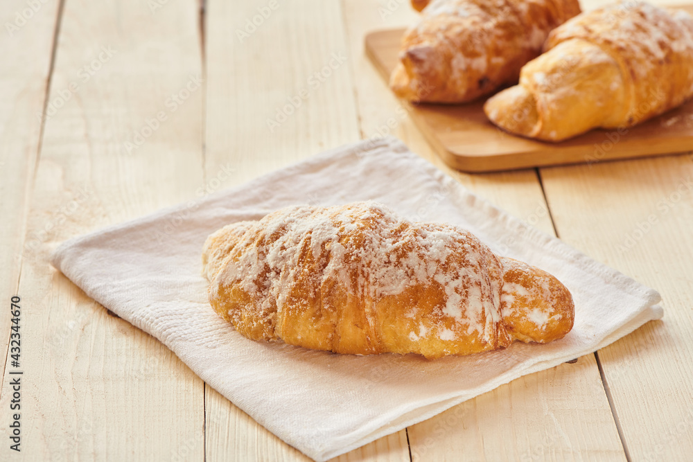 Tasty croissants with powdered sugar on wooden board. Traditional french pastry on the breakfast. Close up view