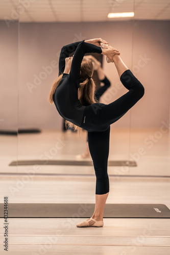 Beautiful young woman is engaged in gymnastics in the gym. The athletic body of the girl is covered with tight-fitting yoga clothes.