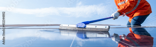 Selective focus mop of technician or worker operating use a mop cleaning solar panels at generating power of solar power plant; technician in industry uniform on level of job description at industrial